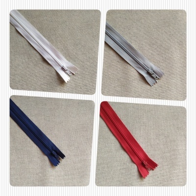 Quatro fechos éclair em branco, cinza, azul e vermelho sobre fundo bege.