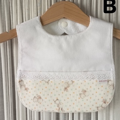 Babete branco com padrão de coelhinhos e botão de pressão pendurado em cabide de madeira