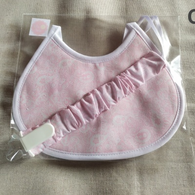 Babete rosa com padrão floral branco embalada em plástico sobre fundo bege