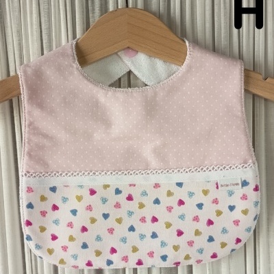 Babete de bebé rosa com padrão de corações coloridos pendurado num cabide de madeira