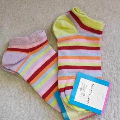 Meias curtas coloridas com riscas e etiqueta de tamanho único sobre fundo cinzento.
