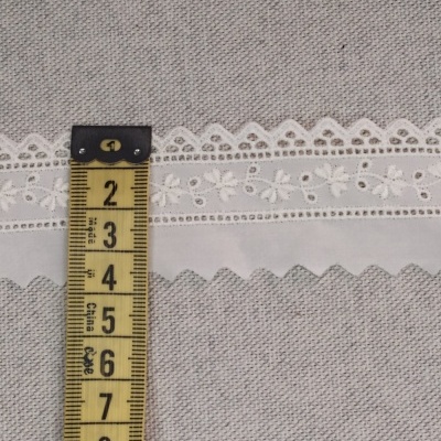 Fita de renda branca floral sobre tecido cinzento com fita métrica amarela