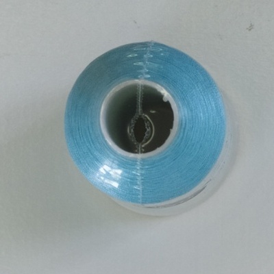 Rolo de linha azul claro embrulhado em plástico sobre superfície branca