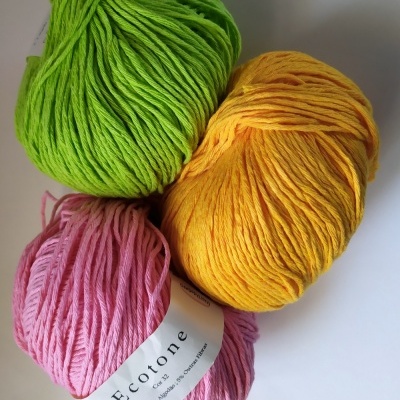 Três novelos de fio de algodão em verde, amarelo e rosa com etiqueta Ecotone