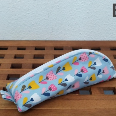 Estojo escolar azul com padrão de flores coloridas sobre madeira