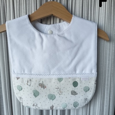 Babete branco e padrão com coelhinhos e balões, pendurado em cabide de madeira