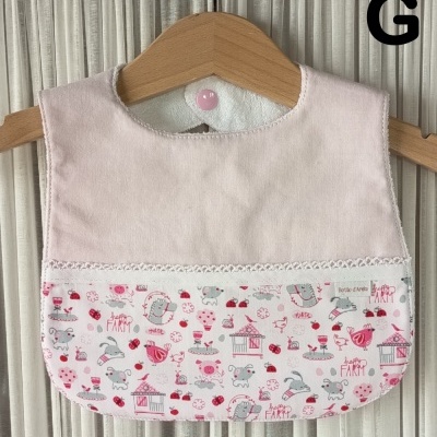 Babete de bebé rosa claro com padrão de quinta pendurado em cabide de madeira