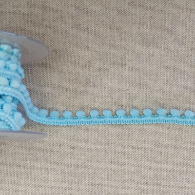 Rolo de fita azul com pompons sobre tecido cinza com texto 'azul'