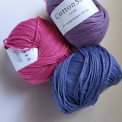 Novelos de lã lilás, rosa e azul com rótulo em fundo branco