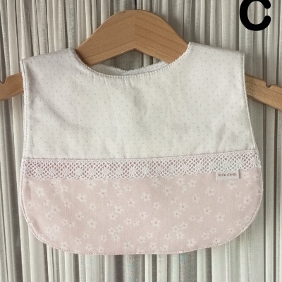 Babete de bebé branco e rosa com renda pendurado em cabide de madeira