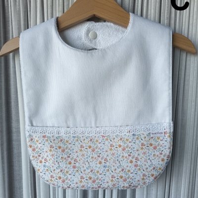 Babete para bebé branco com parte inferior floral e renda pendurado em cabide de madeira