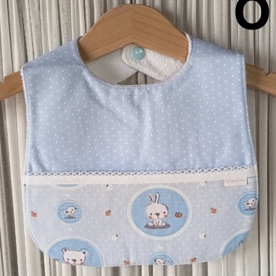 Babete azul claro com padrão de bolinhas e desenhos de animais pendurado num cabide de madeira.