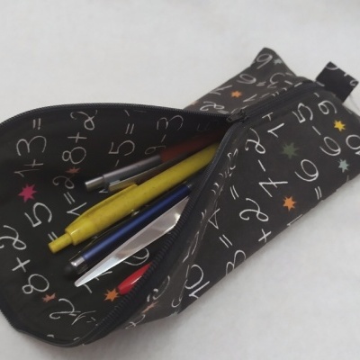 Estojo preto com padrão de números e estrelas coloridas contendo canetas num fundo branco