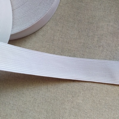 Rolo de fita elástica branca de 30 mm sobre superfície têxtil bege