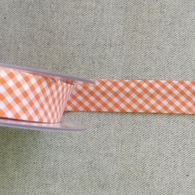 Fita decorativa xadrez laranja e branca em rolo sobre tecido cinza claro