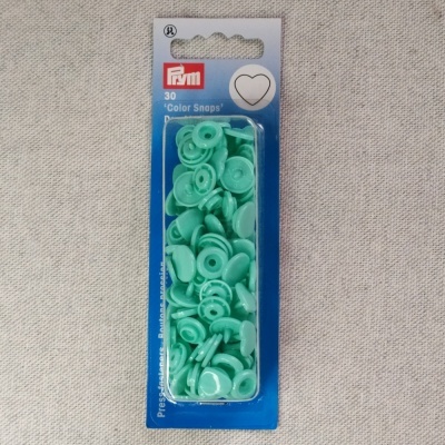 Pacote de botões de pressão verdes da marca Prym em embalagem azul sobre tecido cinza