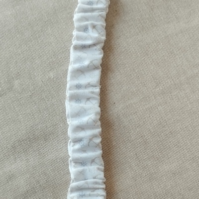 Prendedor de chupeta branco com padrão cinzento e presilha plástica sobre fundo bege