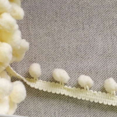 Fita de pompons brancos felpudos sobre tecido cinza.