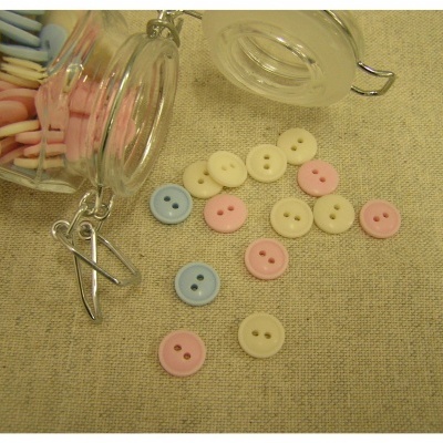 Botões de plástico pastel em frascos de vidro e sobre tecido bege