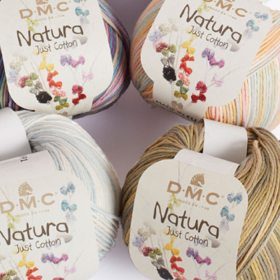 Quatro novelos de lã DMC Natura Just Cotton de cores variadas sobre superfície clara