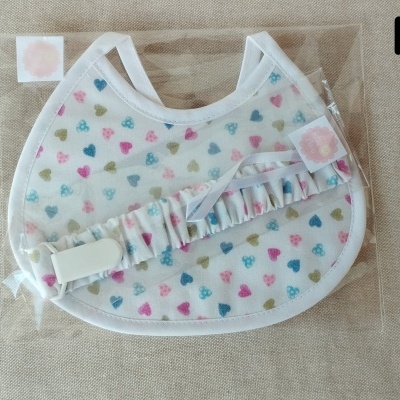 Babete e tira chupeta com padrão de corações coloridos embalados em saco de plástico