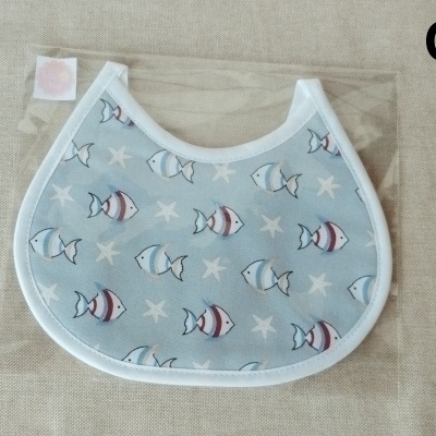 Babete azul claro com padrão de peixes e estrelas do mar em saco plástico