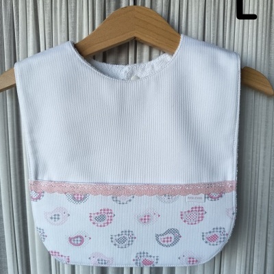 Babete de bebé branco com estampado de pássaros e renda rosa pendurado em cabide de madeira.