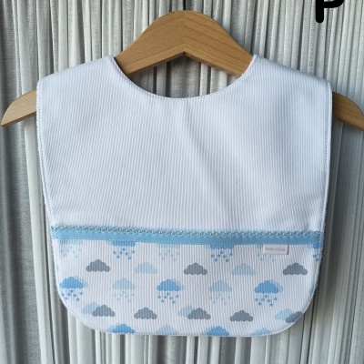 Babete de bebé branco com padrão de nuvens azuis e cinzentas, pendurado num cabide