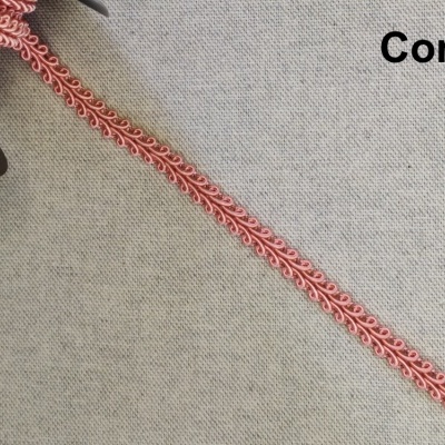 Fita decorativa rosa com padrão de laços finos sobre tecido cinza