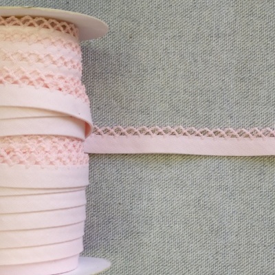 Fita de tecido salmão enrolada em rolo com borda decorativa sobre fundo cinzento