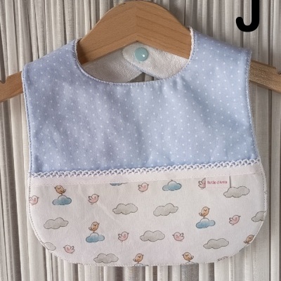 Babete azul claro com bolinhas brancas e parte inferior estampada com nuvens e passarinhos