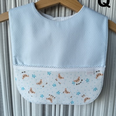 Babete azul claro com padrão de ursos e estrelas pendurado numa cabide de madeira