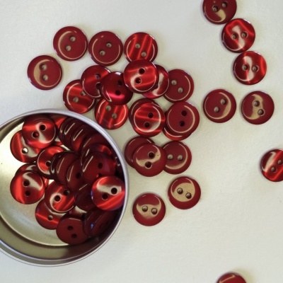 Botões vermelhos de dois furos em superfície branca com caixa metálica aberta