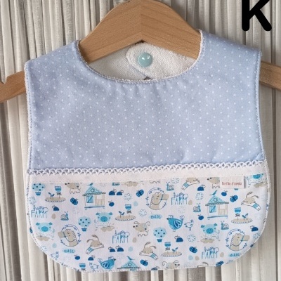 Babete para bebé azul com bolinhas brancas e padrão infantil colorido.
