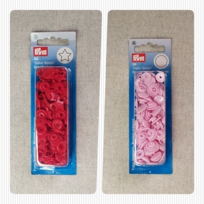 Pacotes de botões de pressão vermelhos e cor-de-rosa da marca PRYM sobre tecido bege