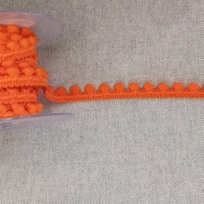 Fita de pompons laranja em carretel sobre tecido cinza
