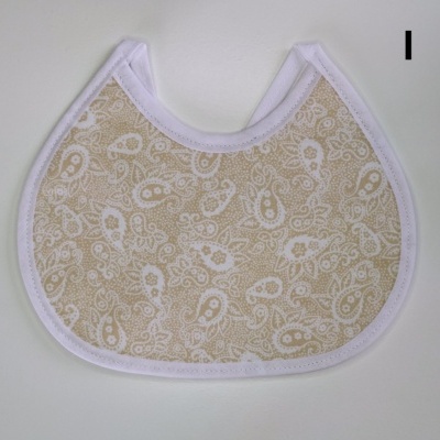 Babeiro bege com padrão branco e borda branca sobre fundo cinzento claro