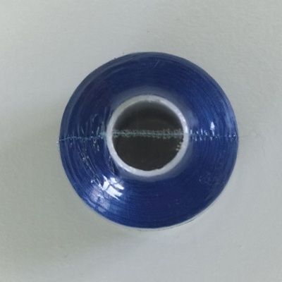Carretel de linha de costura azul com linha passada pelo meio em fundo branco