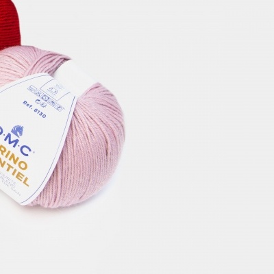 Novelo de lã rosa claro com rótulo DMC Merino Essentiel e outros novelos ao fundo