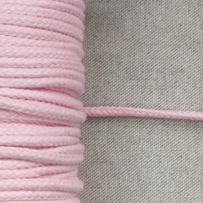 Carretel de fio de algodão rosa claro trançado sobre tecido cinza