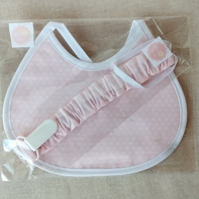 Babete rosa com padrão branco e faixa elástica, dentro de embalagem plástica