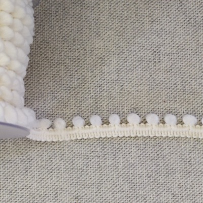 Fita decorativa branca com bolas em carretel sobre tecido cinzento