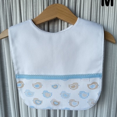 Babete branco com padrão de aves azuis e castanhas pendurado em cabide de madeira