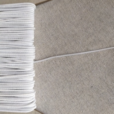 Elástico branco enrolado num cartão sobre tecido bege claro