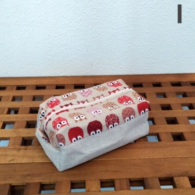 Estojo tecido com padrão de corujas em vários tons de vermelho e castanho sobre base bege, em superfície de madeira.