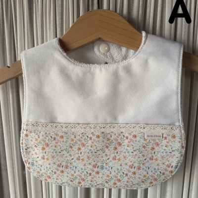 Babete de bebé branco com estampa floral colorida pendurado num cabide de madeira