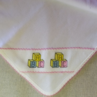 Lenço branco com bordado colorido de cubos com letras e borda rosa, texto PC1 no canto superior direito