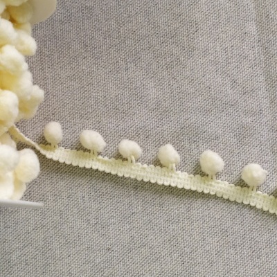 Fita de tecido pérola com bolas felpudas creme sobre fundo cinza