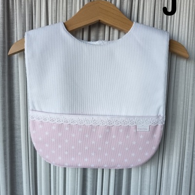 Babete para bebé branco e rosa com renda e estrelas pendurado em cabide de madeira