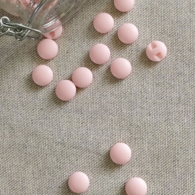 Botões redondos rosa espalhados sobre tecido bege com frasco de vidro ao lado